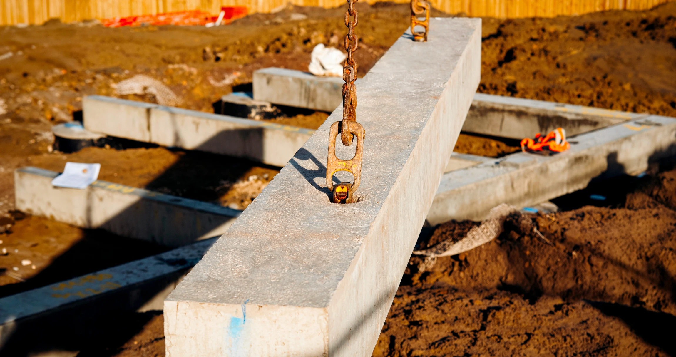 Chantier de construction extérieur avec ouvrier en casque jaune coulant du béton depuis une benne à béton jaune sur ferraillage