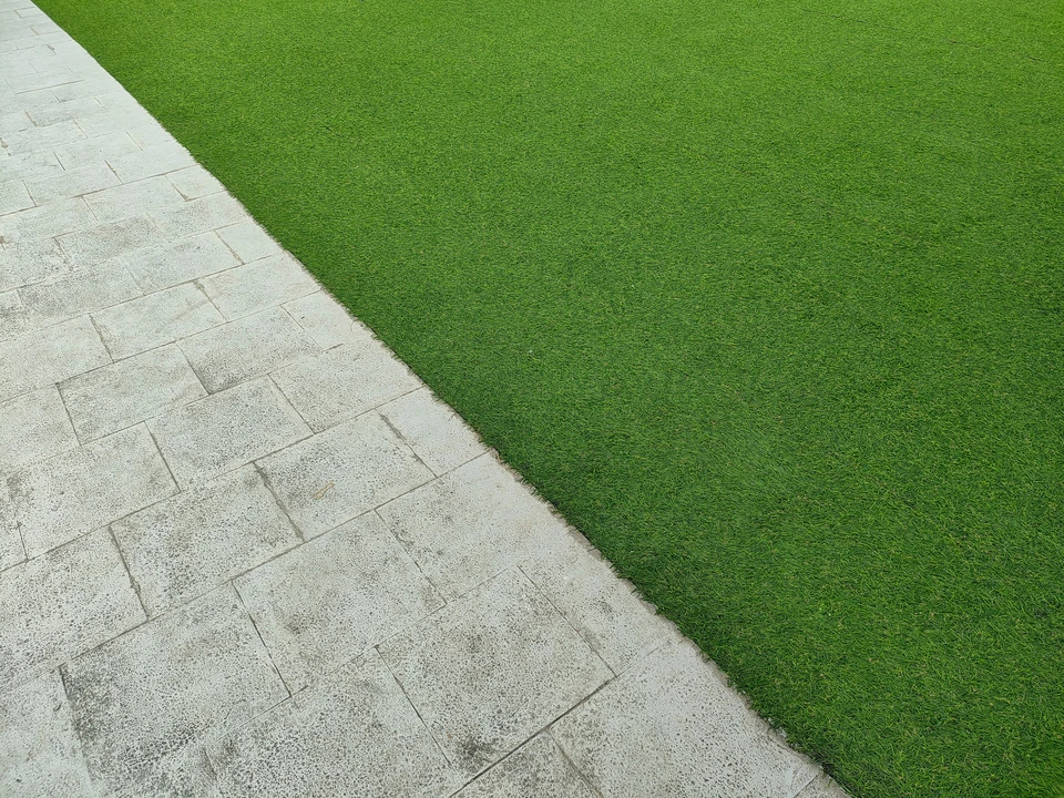 Ouvrier en équipement de sécurité orange et casque blanc installant du pavage extérieur, agenouillé sur dalle béton, utilisant outil de coupe sur pavés gris