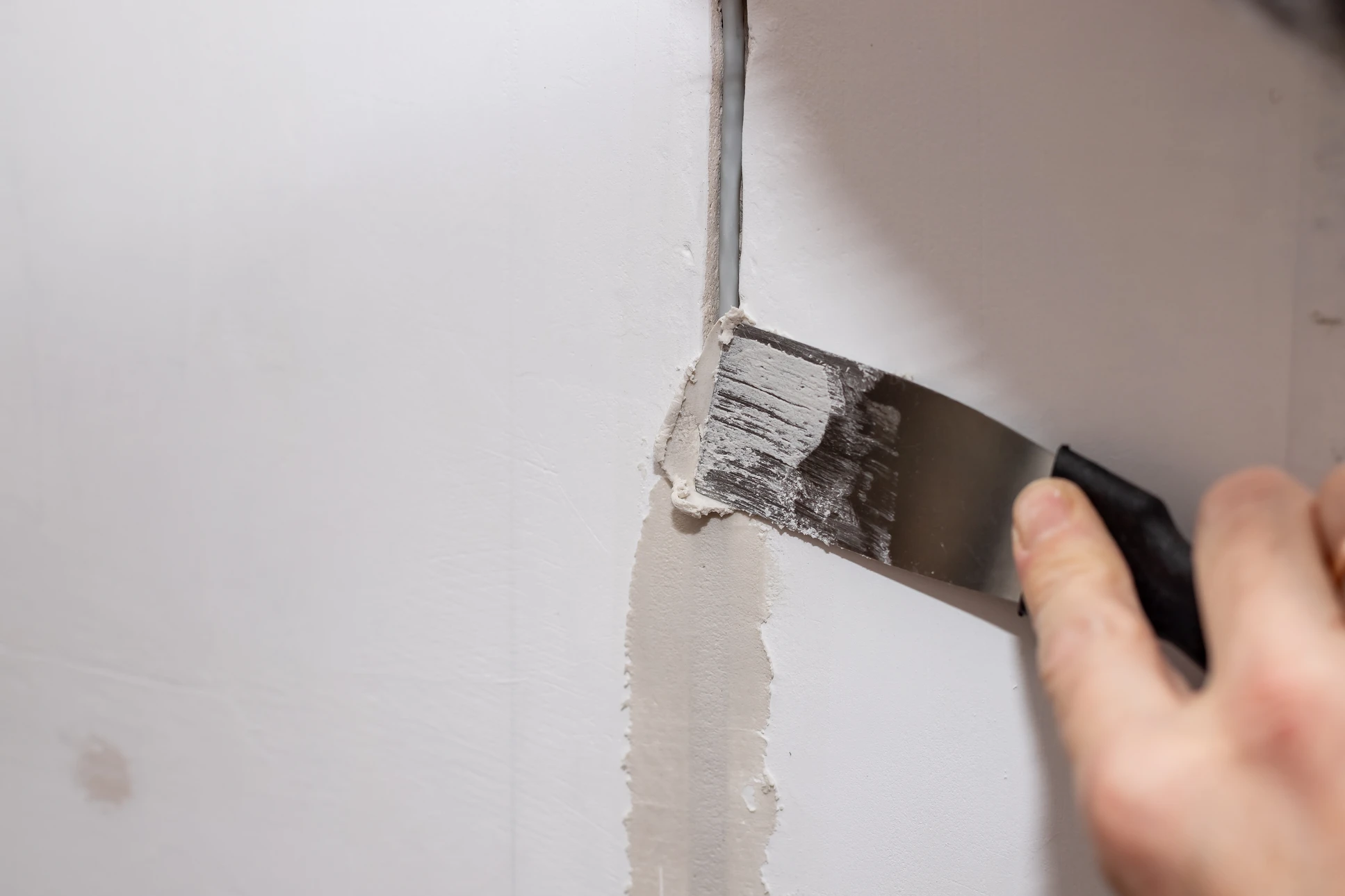 Main à l'extérieur appliquant enduit sur mur blanc avec platoir près d'une fenêtre à cadre bois