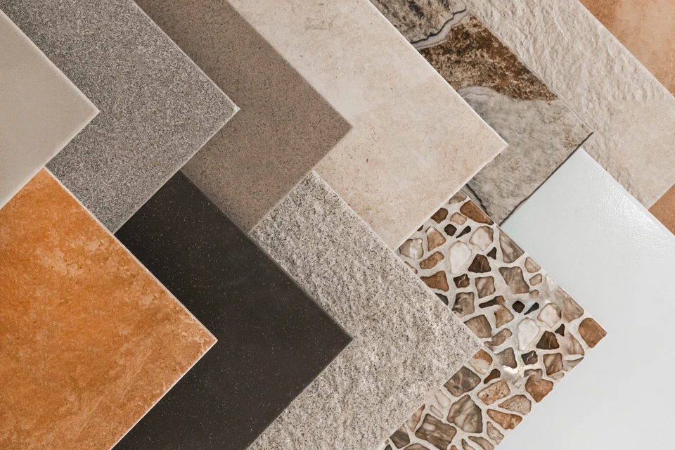 Artisan carreleur à genoux sur chantier intérieur posant carrelage gris au sol