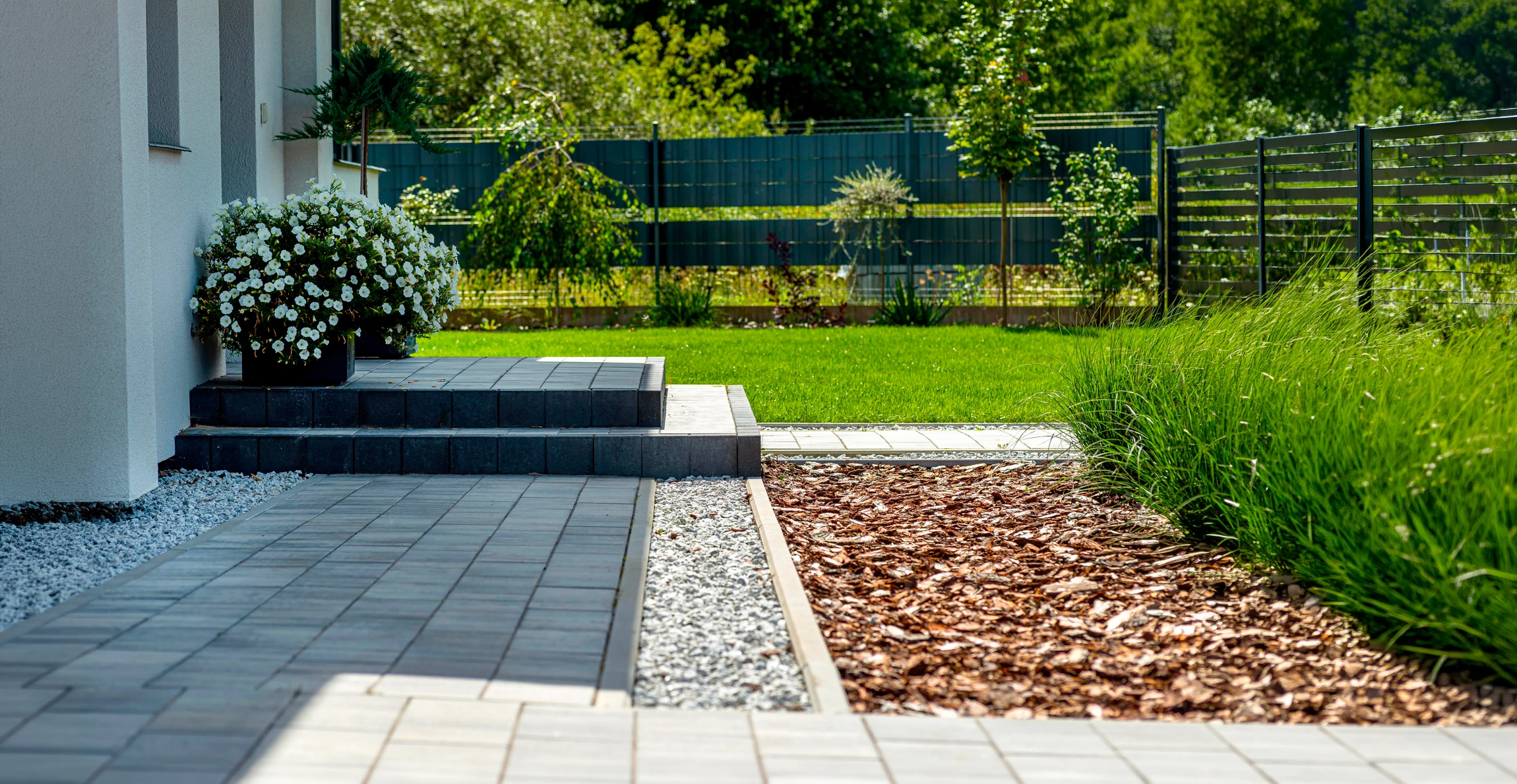 Jardin paysager extérieur avec allée courbe en dalles de grès rose disposées en quinconce sur pelouse verte entretenue